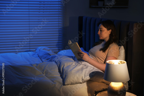 Photography Woman reading book before sleep with night lamp in bed at home