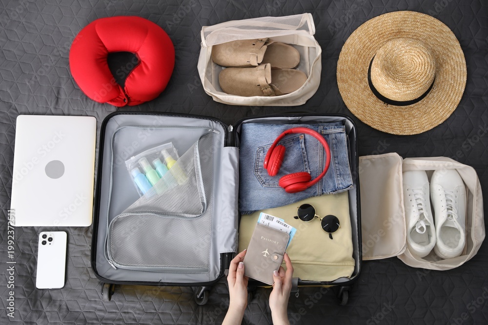 Naklejka premium Woman packing suitcase for trip on bed, top view