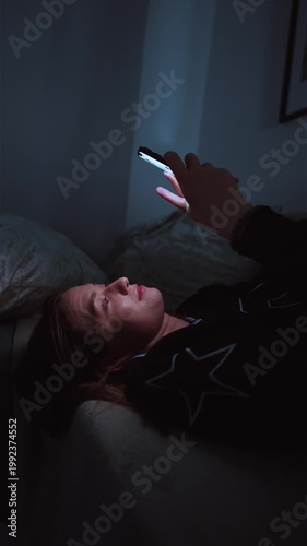 Girl doom scrolling her smartphone on a coach at night. Social network and phone addiction concept. Cozy home ambient light. vertical video