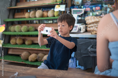 Young Boy Taking Photos at a Market Surrounded by Durian Fruits