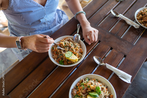 Woman Enjoying Delicious Seafood Noodle Dish Served in a Bowl on a Rustic Wooden Table