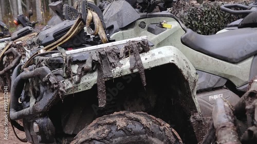 Six-wheeled ATV covered in mud parked among other vehicles in a forested area, showcasing rugged outdoor adventure equipment
