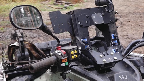 Close-up view of six-wheeler ATV control panel with handlebar, mirror, and buttons in a muddy outdoor setting