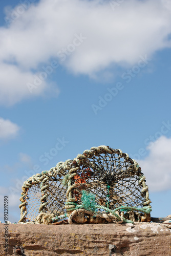 Lobster pot on red stone harbour wall on sunny blue sky day
