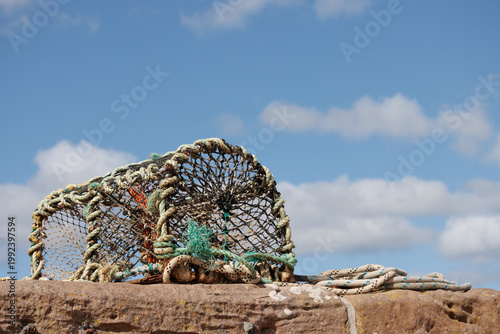 Lobster pot on Scottish stone harbour wall on sunny blue sky day