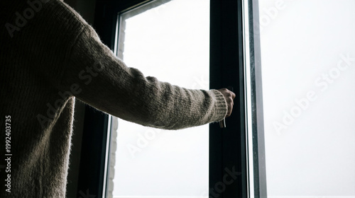 Woman opening glass window frame to look outside. Person standing in room touching handle to ventilate house. Home interior concept of fresh air, freedom, hope, new day and morning light.