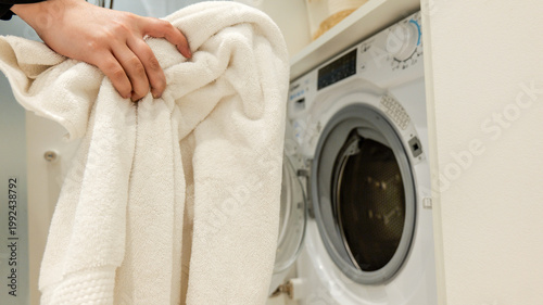 Foto Hand holding a fluffy white towel near an open washing machine door
