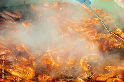 Canvas-taulu Shrimp sizzling in hot pan with oil and steam, street food cooking, close view of seafood preparation