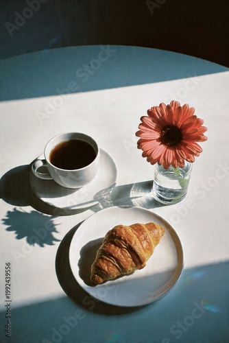 Minimal breakfast flat lay with coffee croissant and flower on white table