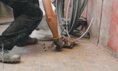 A Caucasian handyman collects construction waste with a dustpan.