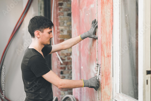 A young Caucasian worker installs a corrugated pipe into a wall.