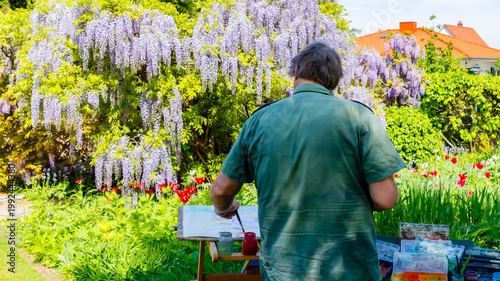 Foto Artist paints under wisteria in a garden with colorful flowers during sunny dayt