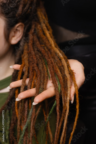 Female hands braiding dreadlocks with decorative threads and beads, close up, front view. Concept hairstyling process, handmade work, beauty service, creative hairstyle design.