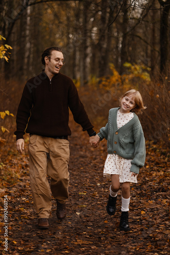 White Father Daughter Walking Autumn Forest, Laughing And Holding Hands, Father Guiding Curious Daughter Along Leafstrewn Path, Cozy Cardigan And Boots, Warm Golden Light, Candid Lifestyle