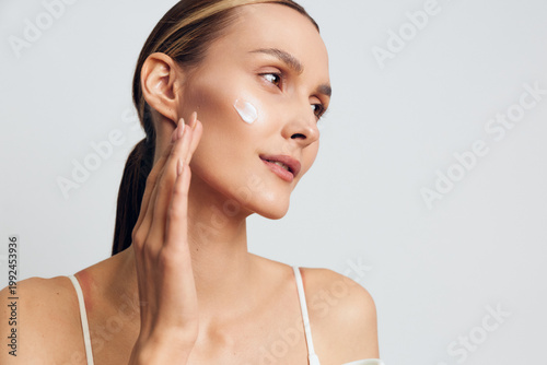 Obraz na plátně Woman applies skincare cream for beauty on her face, moisturizer routine for dai