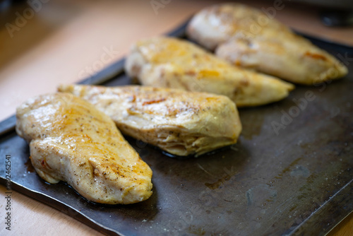 Seared and seasoned chicken breasts on a black baking sheet, to be finished in the oven, cooking a tasty meat dish, copy space, selected focus