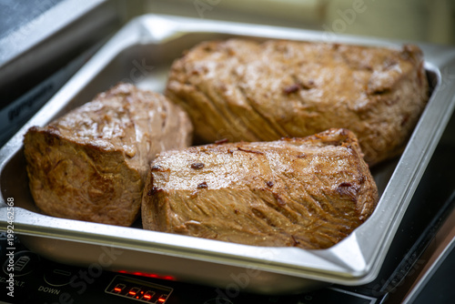 Large pieces of seared veal loin in a stainless steel tray, preparation in a restaurant for the meat course of a dinner menu, selected focus