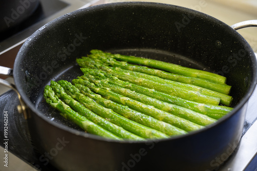 Green asparagus cooked in butter in a black pot on the stove, cooking a healthy vegetarian meal with this delicious spring vegetable, selected focus