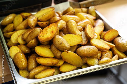 Lots of roasted halved potatoes on a stainless steel tray in a restaurant or a professional food service company, ready to serve as a side dish, selected focus