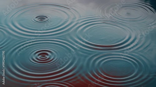Close-up of water with concentric circles, reflecting light. Cool tones over dark red below
