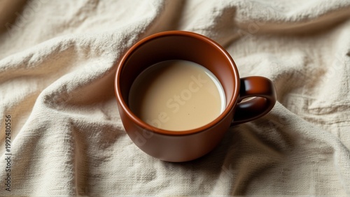 close brown ceramic mug handle beige fabric background mug filled light brown liquid which appears coffee tea fabric has textured pattern slightly wrinkled giving soft cozy feel background blurred