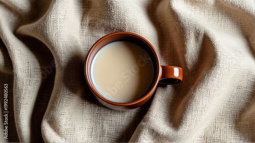 close cup coffee beige fabric cup brown color has handle one side liquid inside cup light beige color appears creamy white color fabric draped over cup creating soft silky texture background blurred