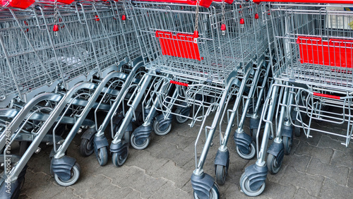 Row of metal shopping carts with red baskets, outdoor storage.
