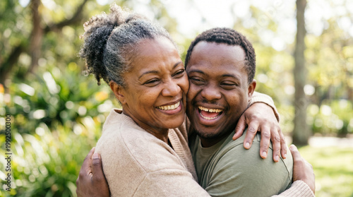 Happy African American mother and her adult son with Down syndrome embracing in a sunny park, family love, inclusive living, diversity.