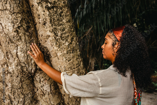 Young woman leans her forehead against a large tree trunk in a quiet moment of reflection