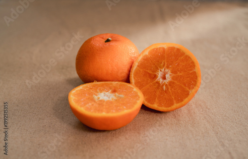 фотографія A fresh orange fruit arrangement placed on a neutral fabric background, featuring one whole orange and two halves cut crosswise to reveal the bright