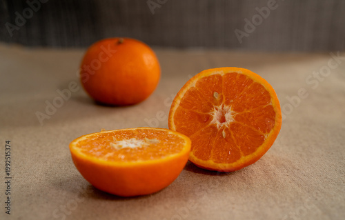 Принти на полотні A fresh orange fruit arrangement placed on a neutral fabric background, featuring one whole orange and two halves cut crosswise to reveal the bright