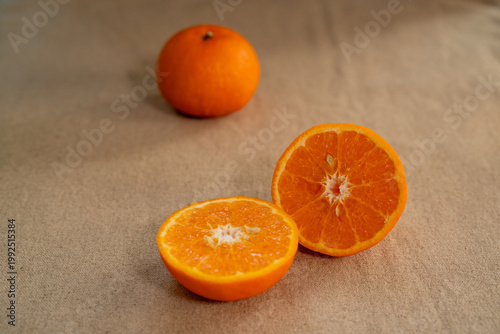 Quadro em tela A fresh orange fruit arrangement placed on a neutral fabric background, featuring one whole orange and two halves cut crosswise to reveal the bright