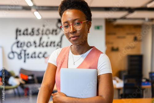 Confident woman holding laptop in modern office