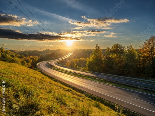 Empty asphalt highway winding through forested landscape in autumn colors at sunset