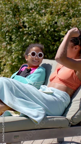 Vertical video: Lifting brown sunglasses mom in coral sharing them with kid in daisy shades by pool