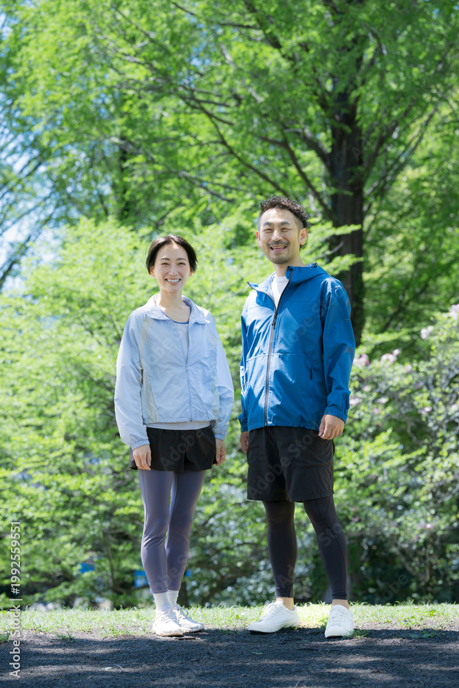 Obraz premium 新緑の公園でウォーキングや散歩を楽しむミドル夫婦の正面全身カメラ目線で笑顔