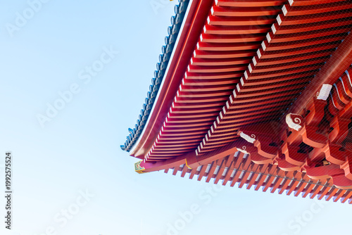 Low angle view of a traditional Japanese Buddhist temple roof with ornate red wooden eaves and blue tiles against a clear blue sky. Detail of Sensoji temple architecture in Asakusa Tokyo Japan.