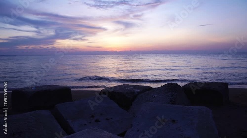 Purple Twilight Sunset Over Calm Sea with Concrete Breakwater Rocks Silhouette on Sandy Beach