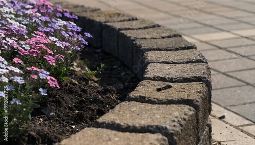 A curved stone border with vibrant flowers in a garden bed alongside a paved walkway