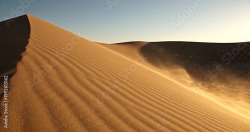 Wind blowing fine golden sand over a tall dune in the desert at sunset