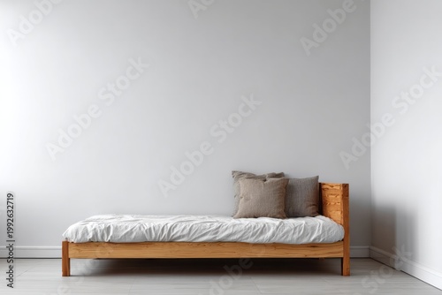 Minimalist wooden bed with pillows sits against a plain wall.