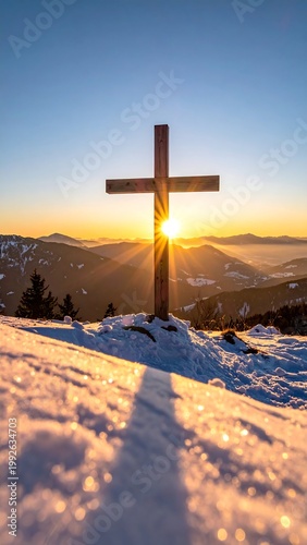 Wooden cross stands on snow-covered peak with sunburst over mountain landscape