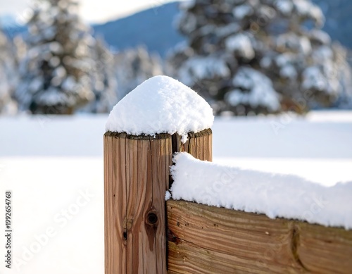 Wooden fence post covered in snow, in a blurry winter landscape