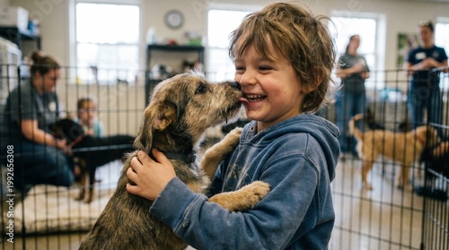 A joyful young boy laughs as a playful dog licks his face inside an animal shelter.