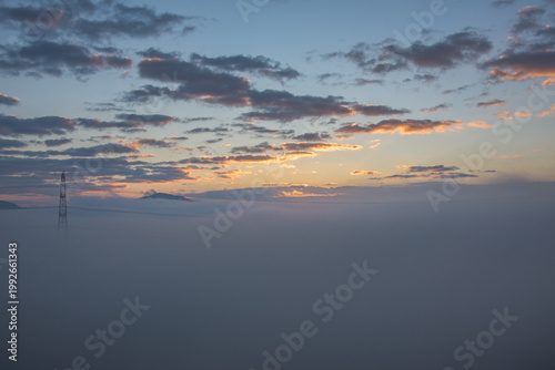 Obraz na plátně Power transmission tower above sea of fog at sunset