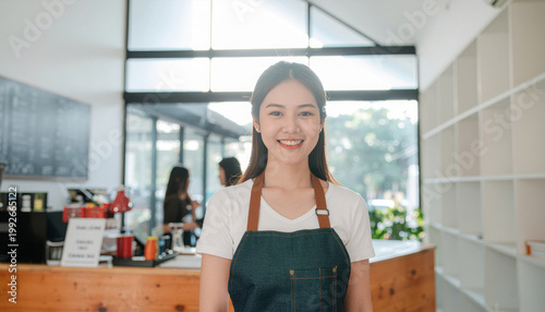 Cheerful young small business owner barista standing in modern coffee shop counter wearing apron smiling with welcoming friendly emotion during service at cafe inside retail store atmosphere