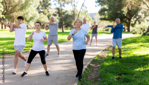 Group of young and elderly people exercising outdoors, focused and happy multiracial individuals performing active fitness stretching and walking park with positive energy and healthy lifestyle
