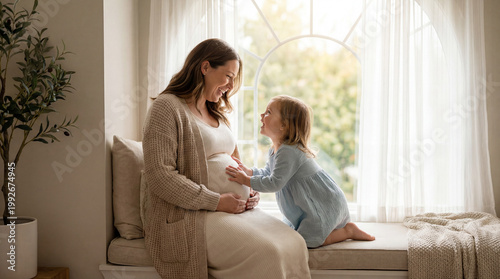 Mother's Day pregnant woman with toddler daughter by window expressing sibling anticipation tenderness for parenting lifestyle magazine editorial content