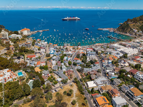 Aerial view of a coastal town with a busy harbor full of boats, winding streets, and a large cruise ship anchored offshore.