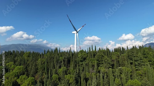 High-angle shot showing the scale of a modern wind generator compared to the surrounding forest in Veneto.
